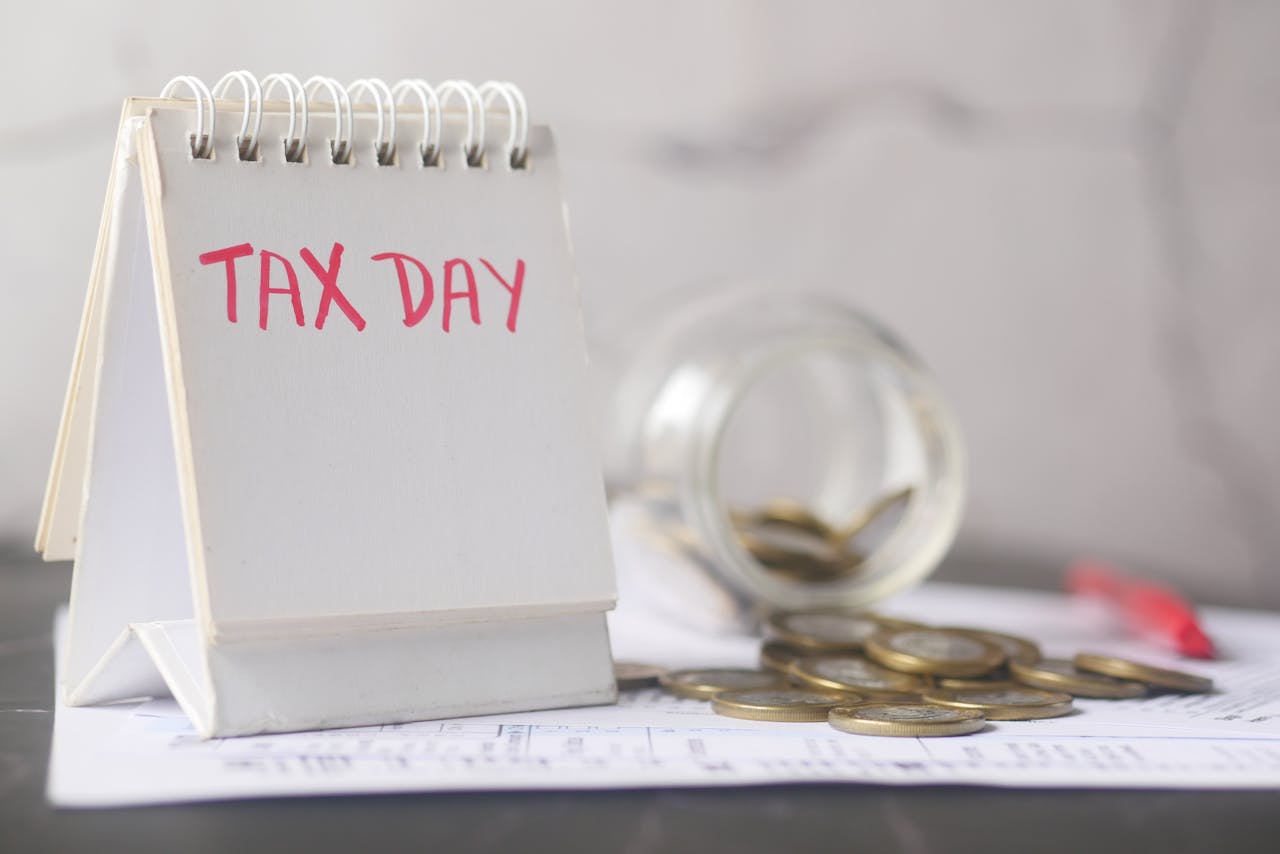 about-us A close-up of a table calendar marked Tax Day with a jar of coins and notes, symbolizing financial planning.
